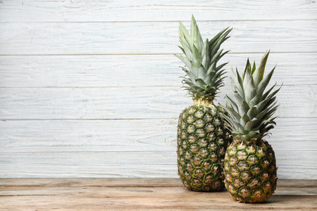 Fresh delicious pineapples on table against wooden background, space for textの写真素材