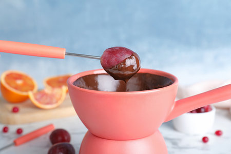 Dipping grape into pot with chocolate fondue on table, closeupの写真素材