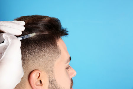 Young man with hair loss receiving problem injection on color background, closeup. Space for textの写真素材