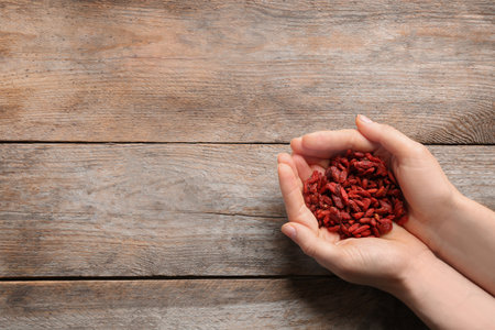 Woman holding red dried goji berries on wooden background, top view. Space for textの写真素材