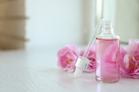 Bottle of rose essential oil, pipette and fresh flowers on window sill, space for textの写真素材