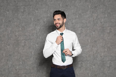 Portrait of businessman straightening tie on gray backgroundの写真素材