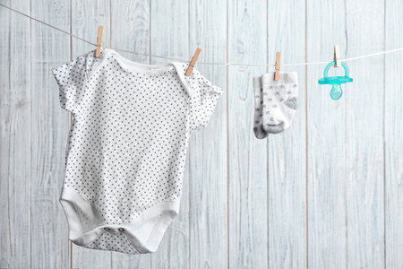 Bodysuit, pair of socks and pacifier on laundry line against wooden background. baby accessoriesの写真素材
