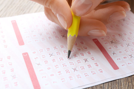 Woman filling out lottery ticket with pencil on wooden table, closeupの写真素材