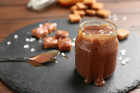 Slate plate with jar of tasty caramel sauce on wooden table. Space for textの写真素材