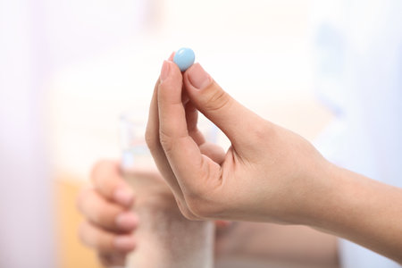 Woman holding pill and glass of water on blurred background, closeup. Space for textの写真素材