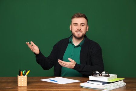 Portrait of young teacher at table against green backgroundの写真素材