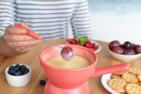 Woman dipping grape into pot with white chocolate fondue at table, closeupの写真素材