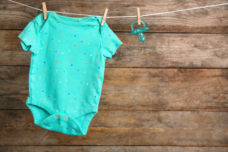 Bodysuit and pacifier on laundry line against wooden background, space for text. baby accessoriesの写真素材