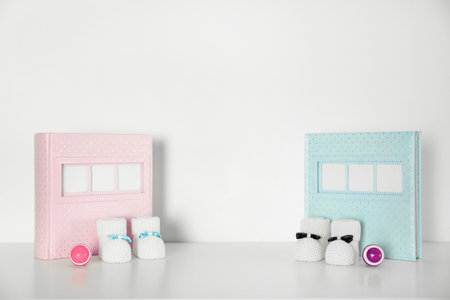 Photo albums with bootees and rattles for baby room interior on table near white wallの写真素材