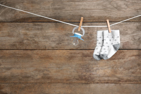 Pair of socks and pacifier on laundry line against wooden background, space for text. baby accessoriesの写真素材