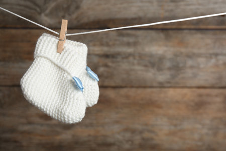Pair of knitted booties on laundry line against wooden background, space for text. baby accessoriesの写真素材