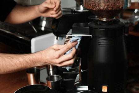 Barista cleaning coffee grinding machine with rag in cafe, closeupの写真素材