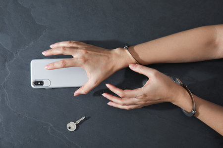 Woman in handcuffs with smart phone on black background, top view. Loneliness conceptの写真素材