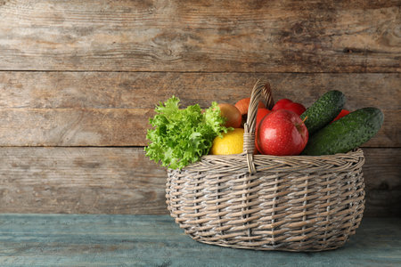 Wicker basket with ripe fruits and vegetables on color wooden table. Space for textの写真素材