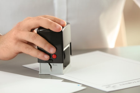 Male notary stamping document at table, closeup