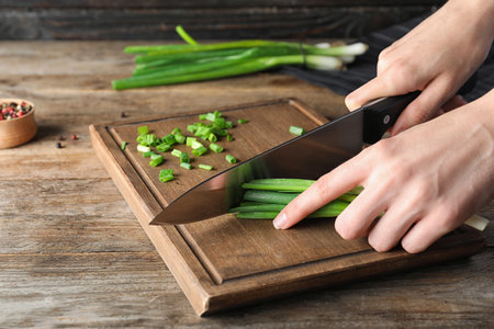 Woman cutting fresh green onion on wooden board at table, closeupの写真素材