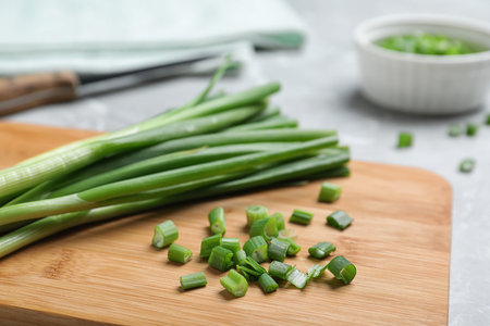 Wooden board with bunch of fresh green onion on table, closeup