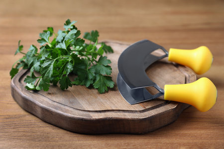 Cutting board with parsley and mezzaluna knife on wooden tableの写真素材