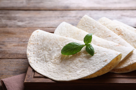 Board of tasty tortillas with basil leaves on wooden table, closeupの写真素材