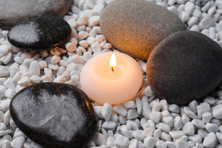 Beautiful burning candle and smooth pebbles on small white stonesの写真素材