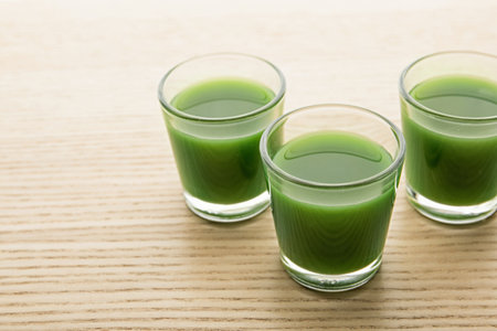Shot glasses of wheat grass juice on wooden table, space for textの写真素材