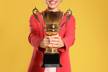 Young businesswoman with gold trophy cup on yellow background, closeupの写真素材