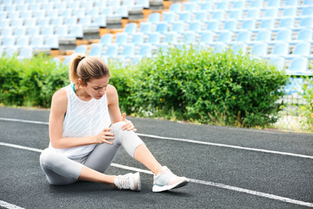 Woman in sportswear suffering from knee pain at stadiumの写真素材