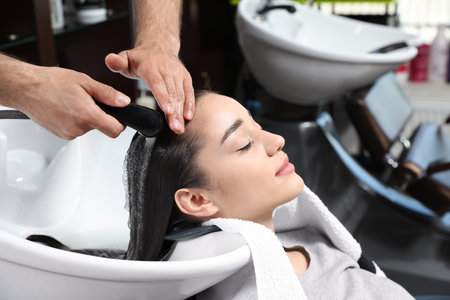 Stylist washing client's hair at sink in beauty salonの写真素材