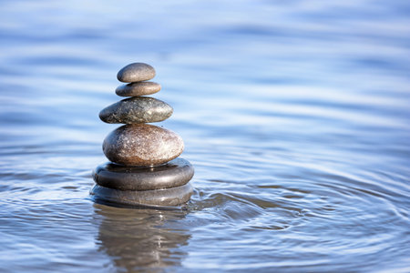 Stack of dark stones in sea water, space for text. Zen concept