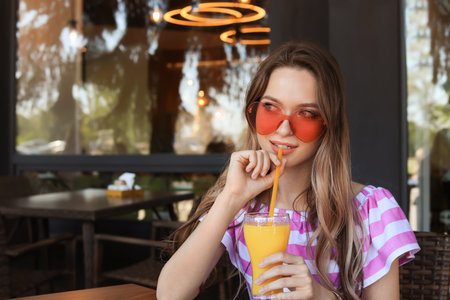 Happy young woman with heart shaped glasses and juice at cafe. Space for textの写真素材