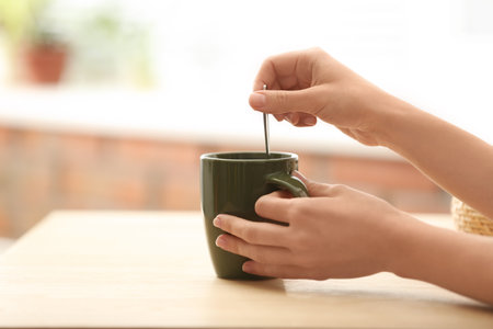 Woman stirring tea with spoon at table indoors, closeup. Space for textの写真素材