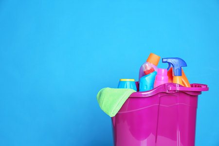 Plastic bucket with different cleaning products against color background. Space for textの写真素材