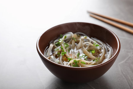Bowl of delicious rice noodles with broth and herb on table