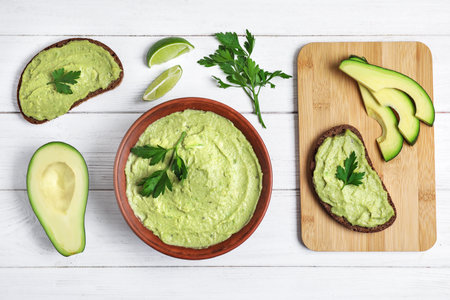 Flat lay composition with bowl of guacamole made of ripe avocados on white wooden tableの写真素材