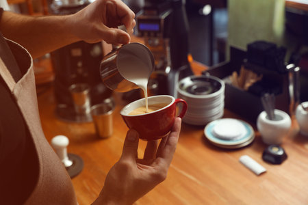 Barista pouring milk into coffee cup at bar counter, closeup. Space for textの写真素材
