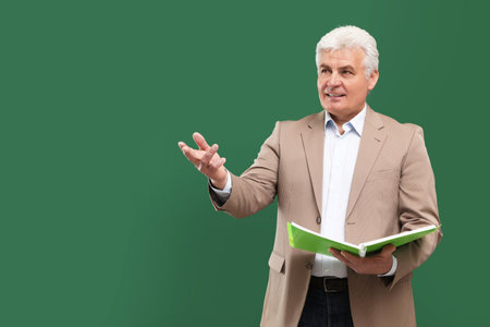 Portrait of senior teacher with notebook at green chalkboard, space for textの写真素材