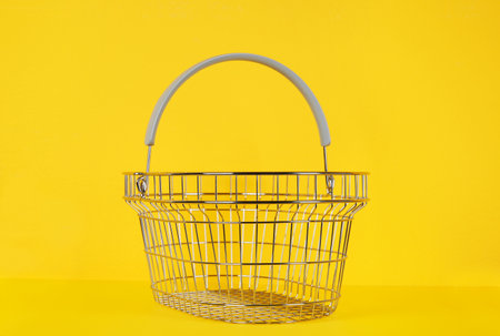 Empty metal shopping basket on yellow backgroundの写真素材