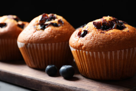 Tasty blueberry muffins on wooden board against black background, closeup viewの写真素材