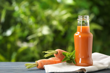Bottle of tasty drink and carrots on table against blurred background, space for textの写真素材