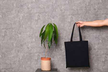 Young man holding eco bag at table with potted plant near gray wallの写真素材