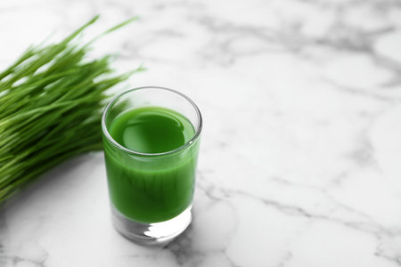 Glass of juice and fresh wheat grass on marble background. Space for textの写真素材