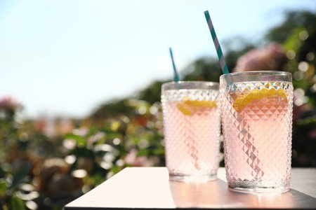 Glasses of pink rose lemonade on table in blooming garden. Space for textの写真素材