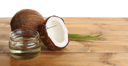 Ripe coconuts and jar with natural organic oil on wooden table against white backgroundの写真素材