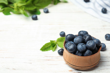 Wooden bowl with tasty blueberries on white table, space for textの写真素材