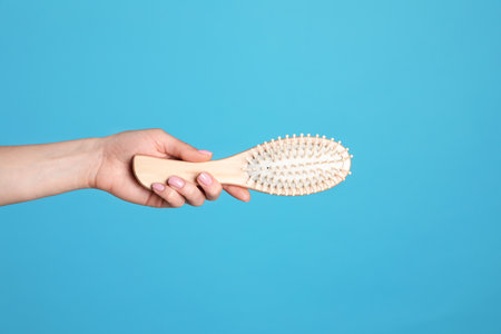 Woman holding wooden hair brush against blue background, closeup