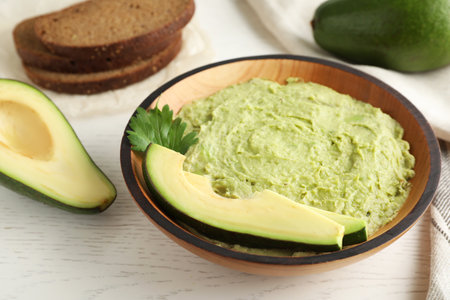 Bowl with guacamole made of ripe avocados served on white wooden table