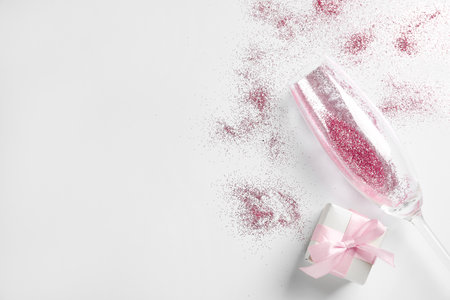 Champagne glass with pink glitter, gift box and space for text on white background, top view. Hilarious celebrationの写真素材