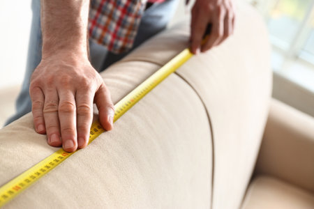 Man measuring beige sofa, closeup. construction toolの写真素材