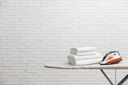 New modern iron and clean towels on board near brick wall, space for text. laundry dayの写真素材